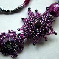 Lynn Davy beading. Purple Passion choker. Featuring rich plum coloured Murano glass, gemstone chips and a variety of beads in a freeform design decorated with brickstitched flowers. The beaded toggles fasten together with a pretty butterfly loop. There is a matching bracelet and a set of flower earrings.